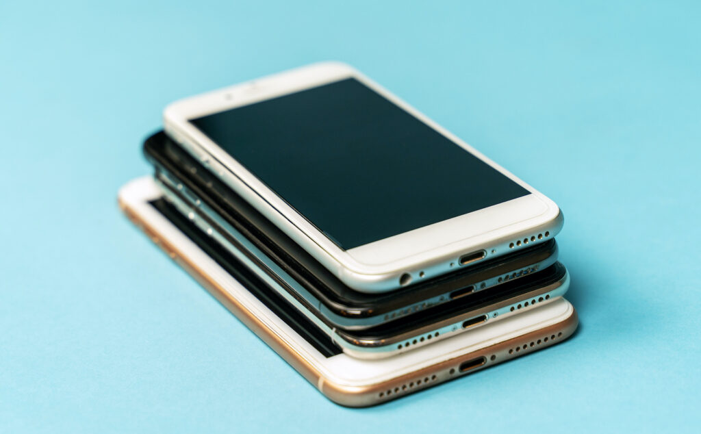 Pile of used old models of mobile phones, black and white, lying down on blue background. Copy space.